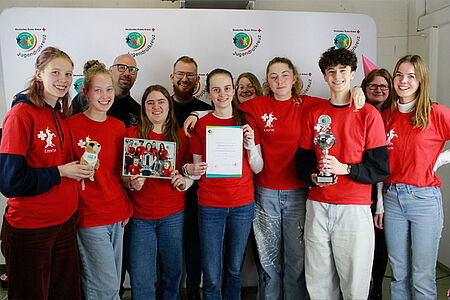 In rot gekleidete Schülerinnen und Schüler mit Urkunden und Pokal.