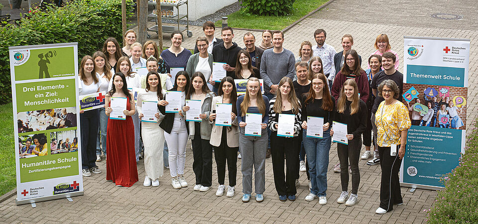 Gruppenbild der Teilnehmer mit ihren Zertifikaten zwischen zwei Roll-Ups.
