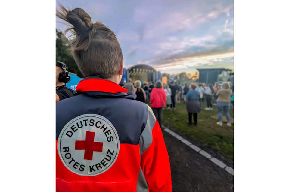 Rotkreuz-Sanitäterin blickt auf ein Festivalgelände mit großer Bühne.