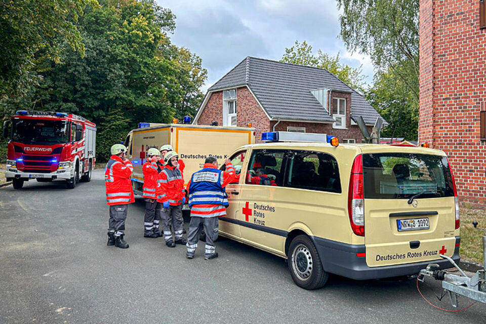 Der Gruppenführer Betreuungsdienst mit blauer Weste bespricht sich mit dem Fahrer eines Einsatzfahrzeugs.