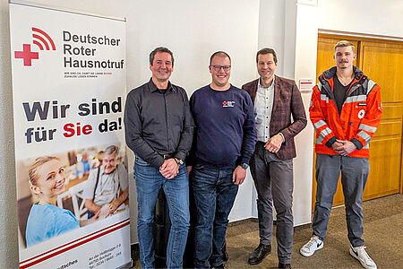 Vier Männer stehen neben einem Rollup des DRK-Hausnotrufs Bochum.