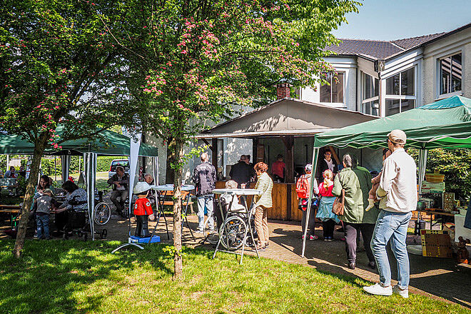 Menschen schlendern an Pavillons und einer Grillhütte vorbei.