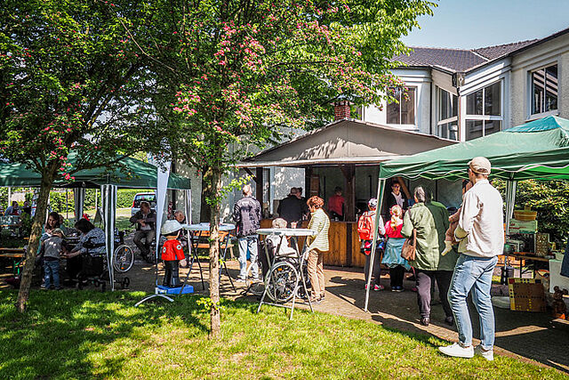 Menschen schlendern an Pavillons und einer Grillhütte vorbei.