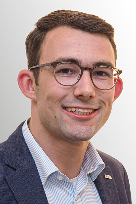 Junger Mann mit dunklen Haaren und Seitenscheitel sowie Brille.