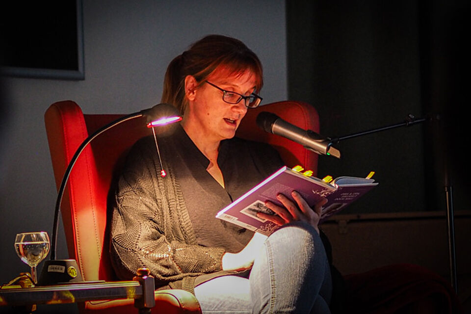 Frau im Sessel liest aus einem Buch.