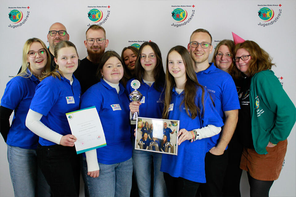 In blau gekleidete Schüler mit Urkunden und Pokal.