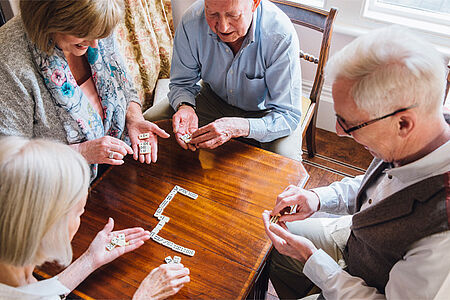 Vier ältere Menschen spielen Domino, fotografiert von schräg oben.