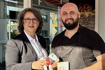 Eine Frau mit Locken und Brille und ein Mann mit Bart und Glatze lächeln.