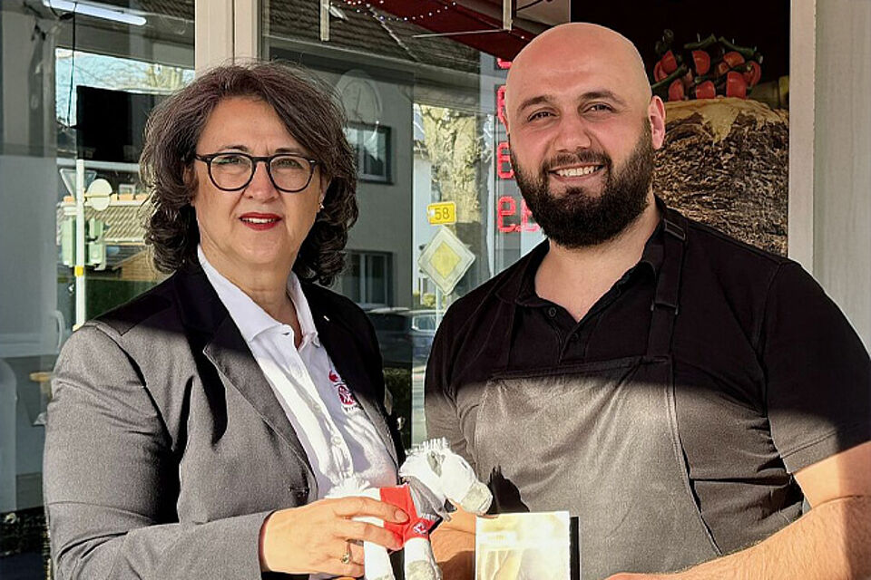 Eine Frau mit Locken und Brille und ein Mann mit Bart und Glatze lächeln.