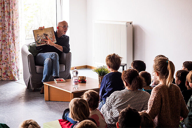 Mann zeigt Kindern ein Buch mit Bildern, aus dem er vorgelesen hat.