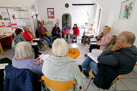 Ältere Menschen sitzen im Kreis vor einer Gitarristin und singen von Notenblättern.
