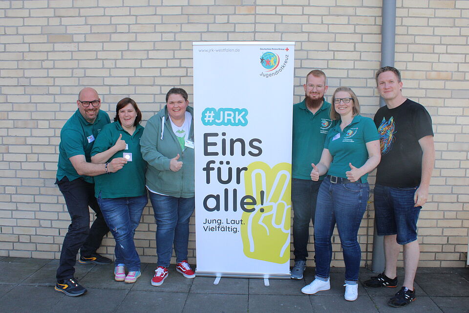 Sechs Menschen neben einem Rollup des Jugendrotkreuz mit dem Slogan "Eins für alle".