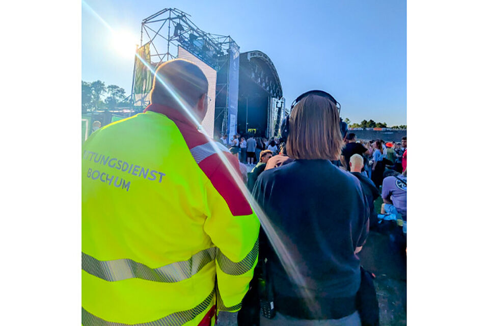 Zwei Rettungssanitäter blicken auf die Menschenmenge, die vor einer großen Festival-Bühne steht.