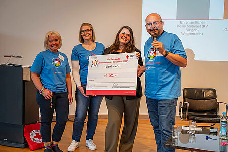 Vier Menschen halten einen großen Scheck hoch.