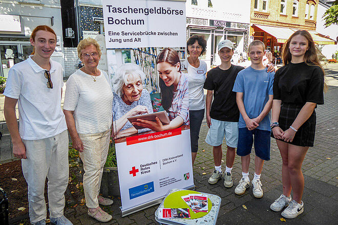 Sechs Menschen stehen um einen Aufsteller der Taschengeldbörse Bochum.
