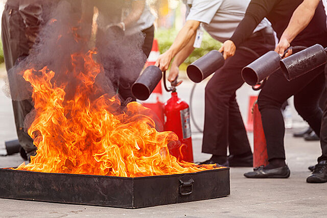 Mehrere Menschen löschen ein Feuer mit einem Feuerlöscher