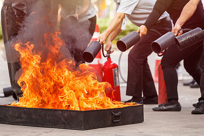 Mehrere Menschen löschen ein Feuer mit einem Feuerlöscher