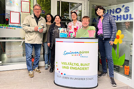 Sechs lachende Menschen hinter einer Infotheke.