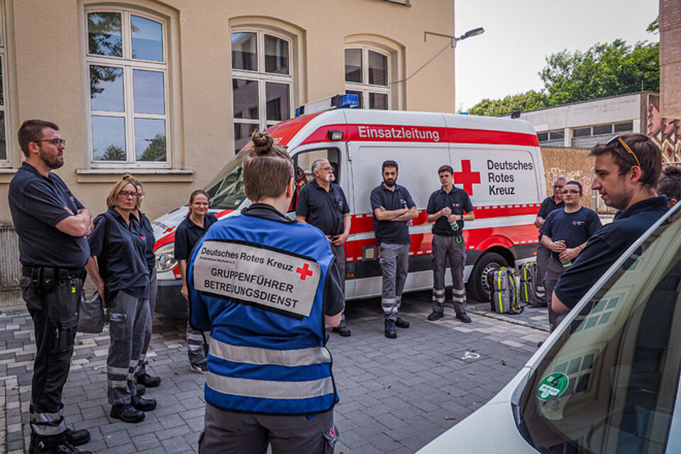 DRK-Helfer und -helferinnen stehen im Kreis und sehen die Gruppenführerin an.