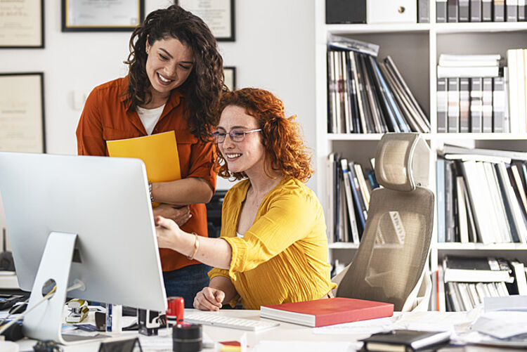 Zwei Frauen zeigen im Büro auf einen Computerbildschirm.