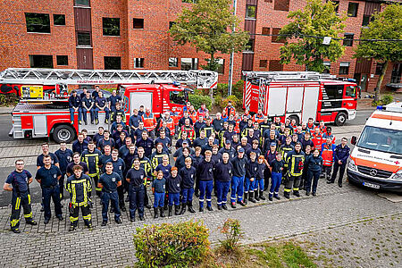 Gruppenbild von rund 100 Feuerwehrleuten und DRK-Helfern vor Löschzug und Krankenwagen.