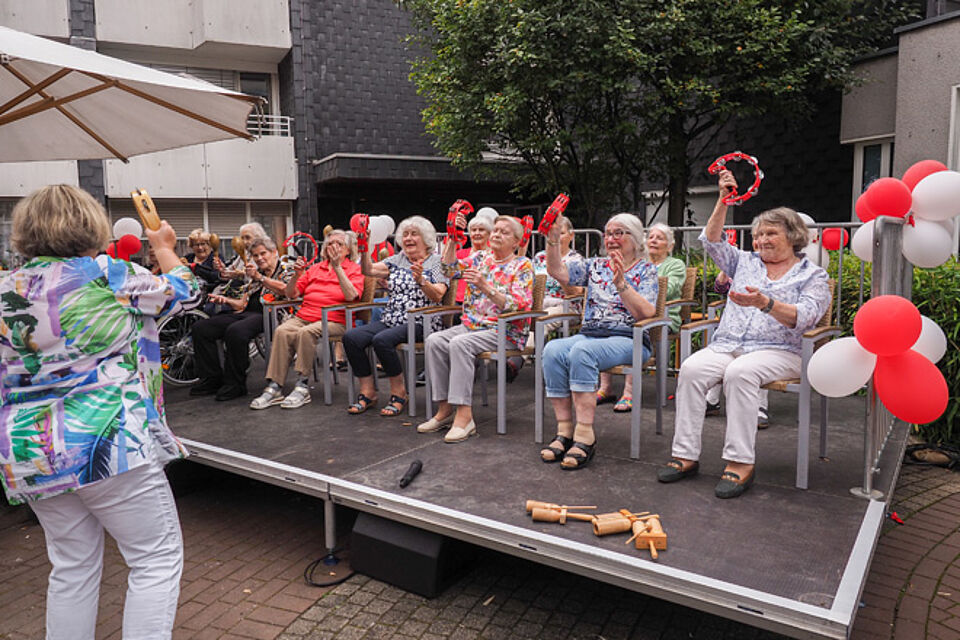 Ältere Menschen auf einer Bühne schwenken Schellenkränze