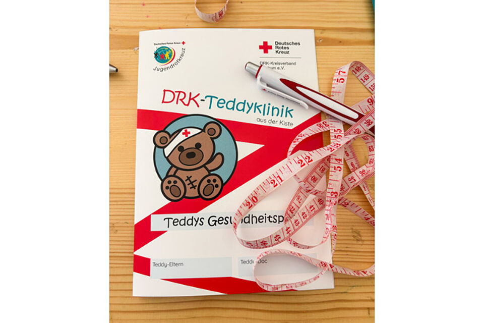Teddyklinik-Gesundheitspass mit Kugelschreiber und Maßband.