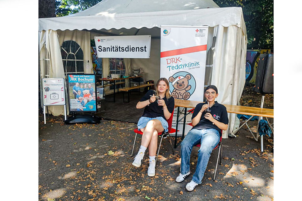 Zwei JRK-Helferinnen sitzen mit kühlen Getränken vor dem Pavillon der Teddyklinik.