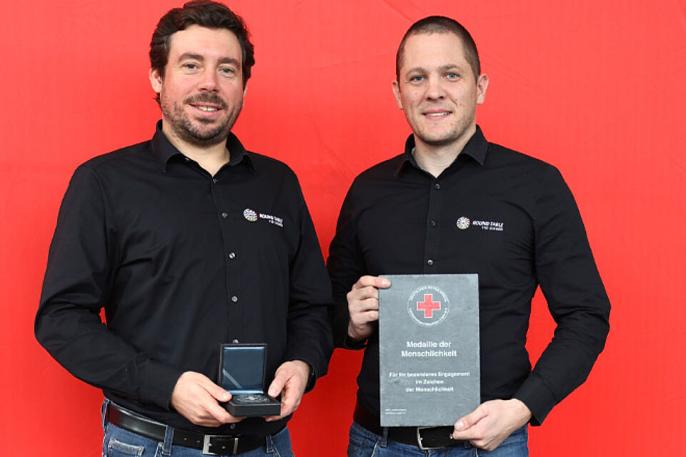 Zwei Männer halten eine Medaille der Menschlichkeit.