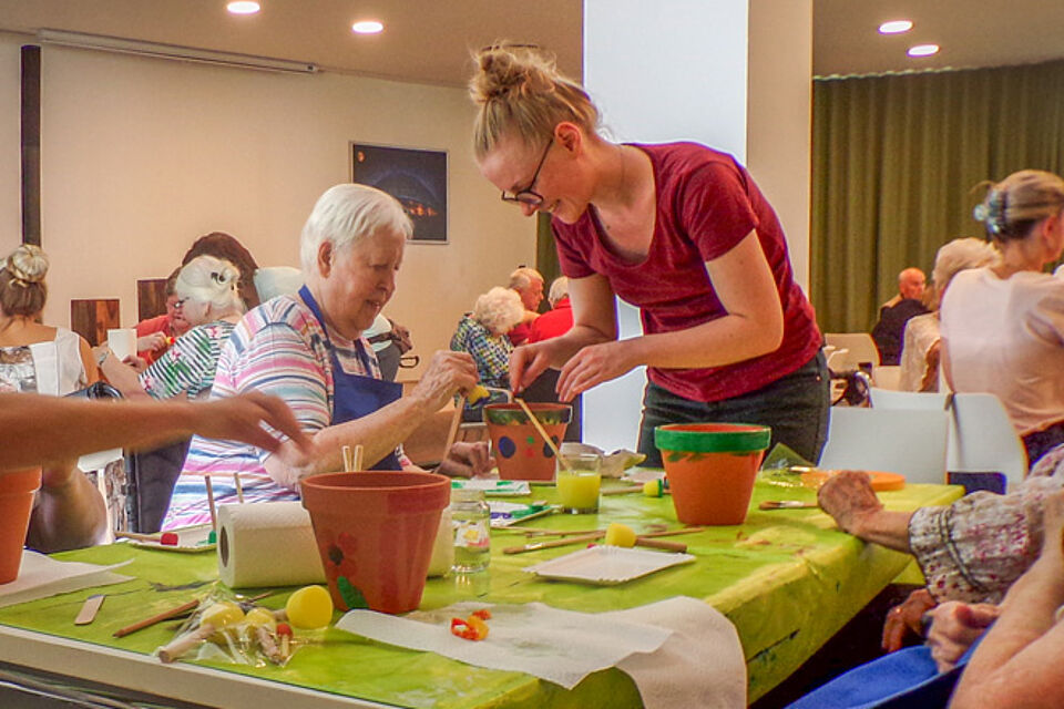 Junge Dame hilft Seniorin beim Tontopf-Bemalen.