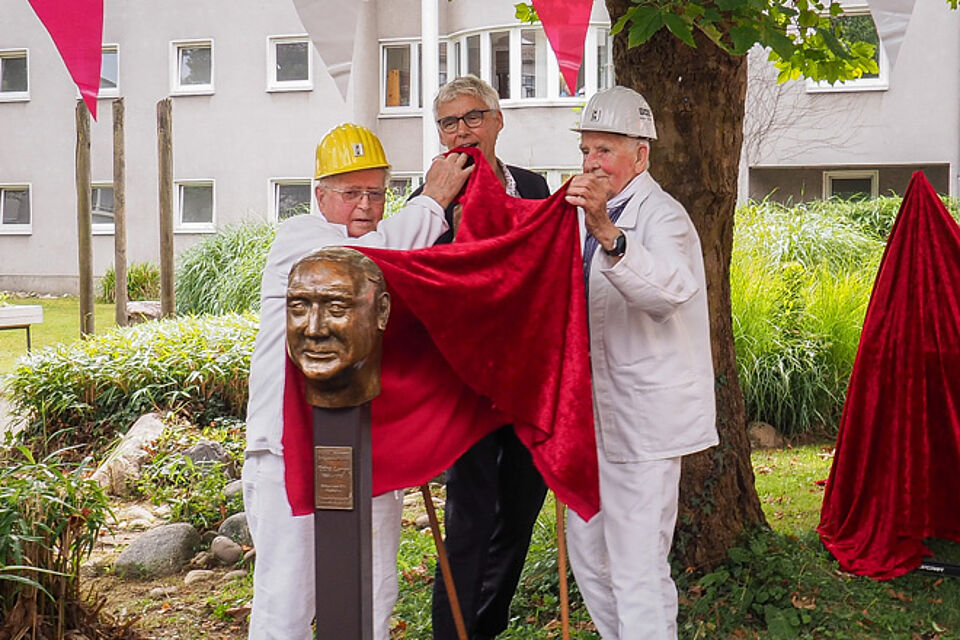 Drei Männer ziehen ein rotes Tuch von einer Bronzeskulptur.