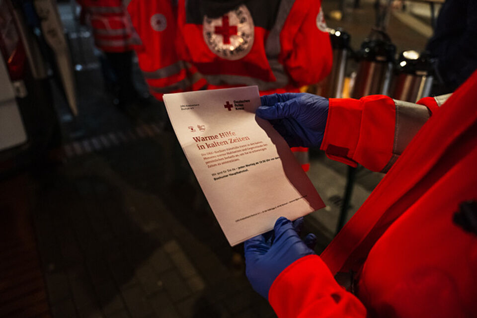 Ein Mann hält ein Flugblatt der DRK-Kältehilfe.