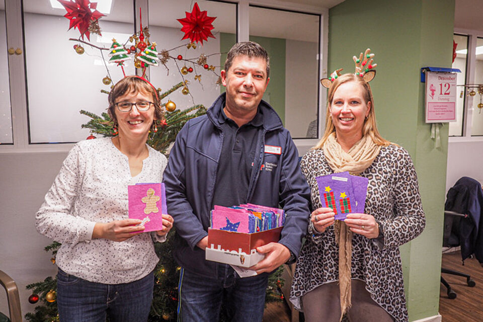 Zwei Frauen und ein Mann zeigen gebastelte Weihnachtskarten.
