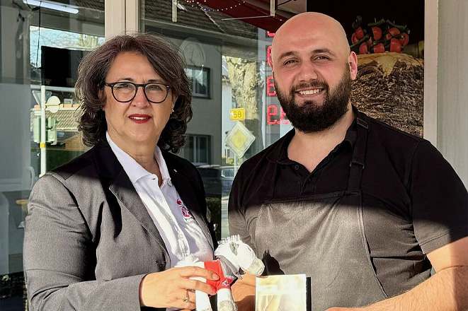 Eine Frau mit Locken und Brille und ein Mann mit Bart und Glatze lächeln.