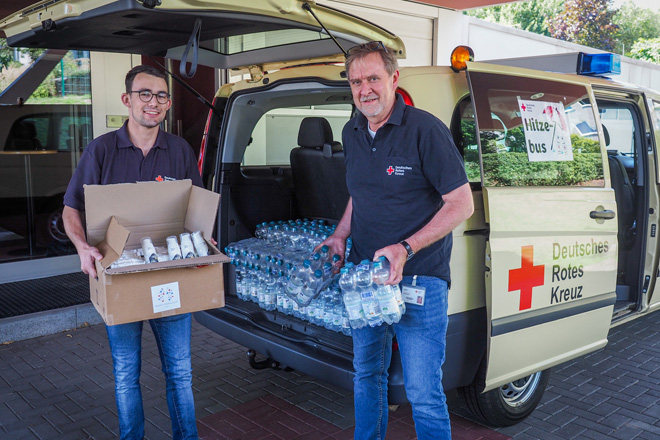 Zwei Helfer des DRK beladen einen Bus mit Wasser und Sonnencrème für Obdachlose.