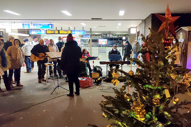 Menschen singen am Bahnhofseingang in Bochum, rechts ein Weihnachtsbaum.