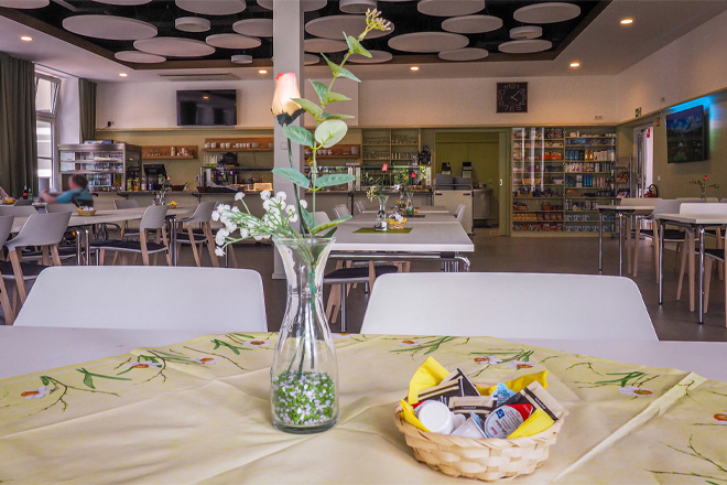 Blick in das Bistro des "Haus der Generationen. Im Vordergrund ein Tisch mit Blume im Hintergrund Tische und die Verkaufstheke.