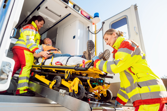 Zwei Notfallsanitäterinnen schieben einen Mann auf einer Trage in einen Rettungswagen.