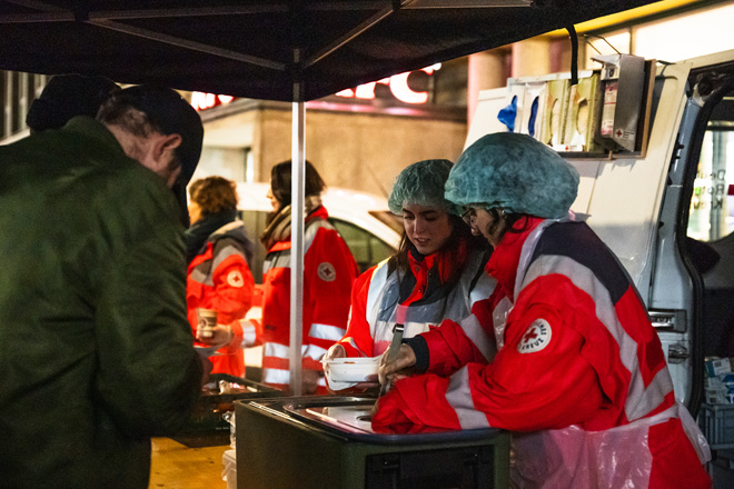 Zwei Helferinnen des Roten Kreuzes geben Suppe an einen Obdachlosen aus.