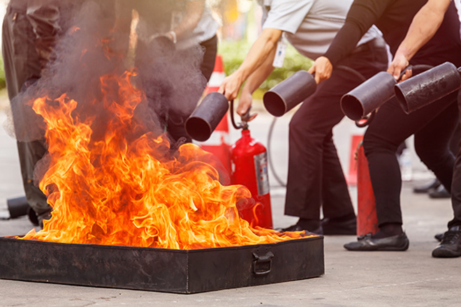 Mehrere Menschen löschen ein Feuer mit einem Feuerlöscher