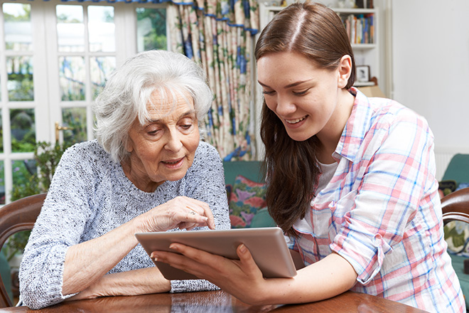 Jüngere hilft ältere Dame bei der Bedienung eines Tablets