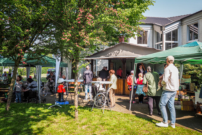 Menschen schlendern an Pavillons und einer Grillhütte vorbei.