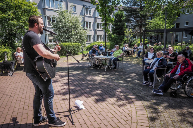 Mann mit Gitarre spielt draußen vor sitzenden Gästen.