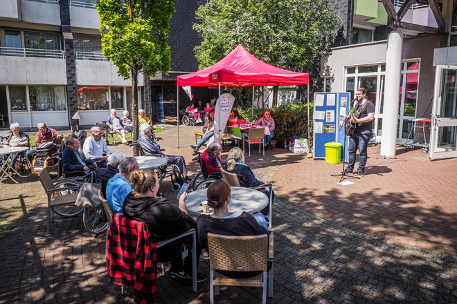 Mann mit Gitarre spielt draußen vor sitzendem Publikum